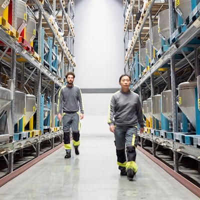 A man and a woman in work clothes walking between two warehouse shelves