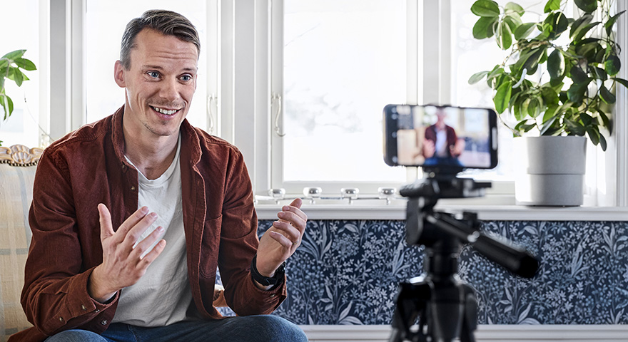 A man looking in to a mobile phone on a stand while the camera is filming him