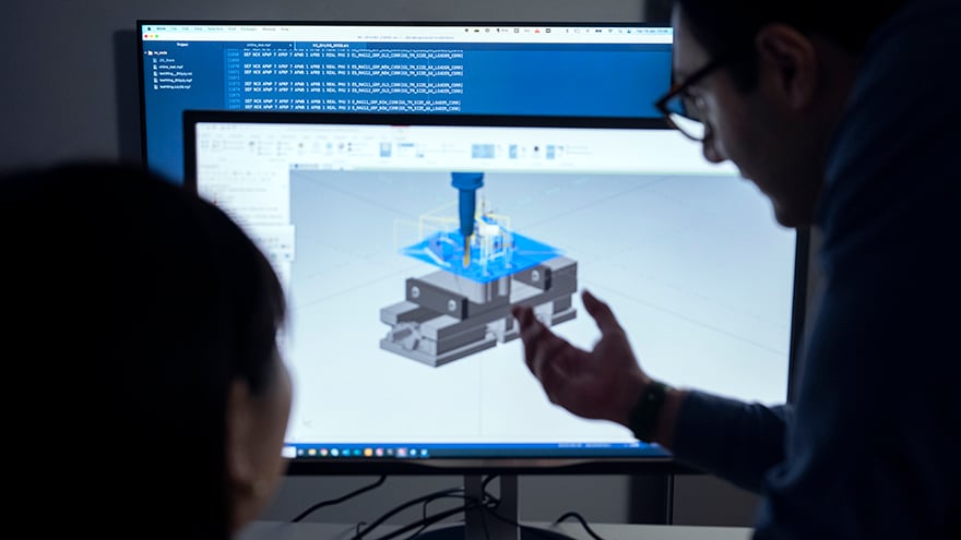 The heads of a woman and a man next to a computer screen displaying software simulating machining operation