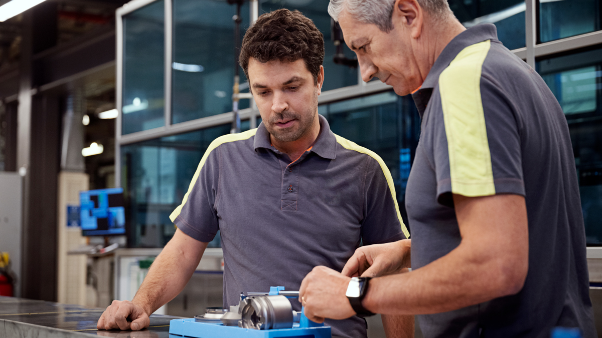 Two men in a production setting. One of them is performing a measuring operation while the other is watching.